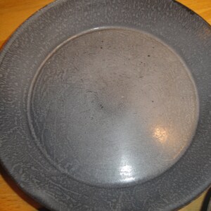 Puede incluir: Un molde para tartas de metal gris con un acabado moteado. El molde tiene un borde ligeramente elevado y una superficie lisa y reflectante.