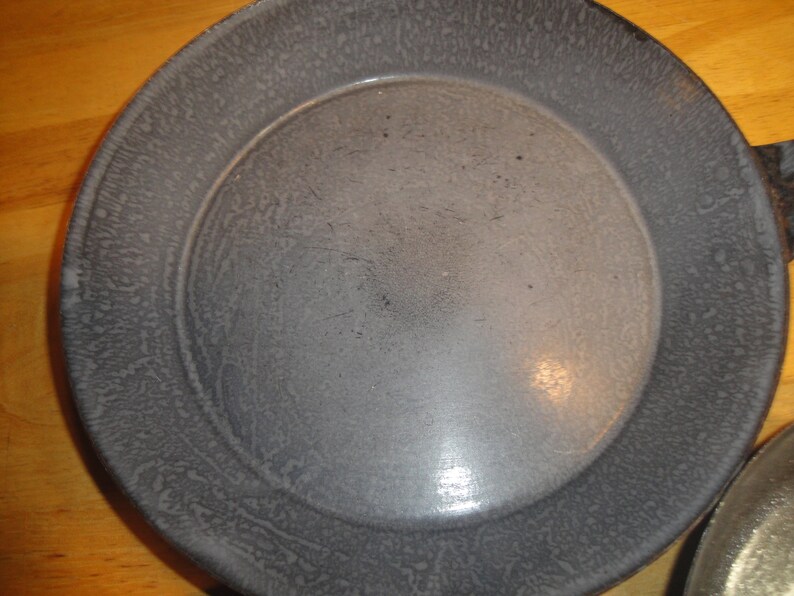Puede incluir: Un molde para tartas de metal gris con un acabado moteado. El molde tiene un borde ligeramente elevado y una superficie lisa y reflectante.