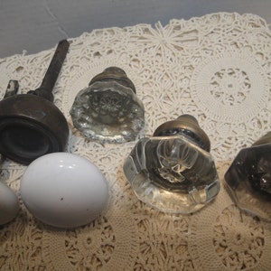 May include: Five antique door knobs, two are white porcelain, three are clear glass with a faceted design. The knobs are arranged on a white crocheted doily.