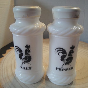 Pode incluir: Saleiro e pimenteiro de cer&acirc;mica branca com um design de galo preto. Os saleiros t&ecirc;m um design de corda em torno do meio e dizem "SALT" e "PEPPER" na parte inferior.