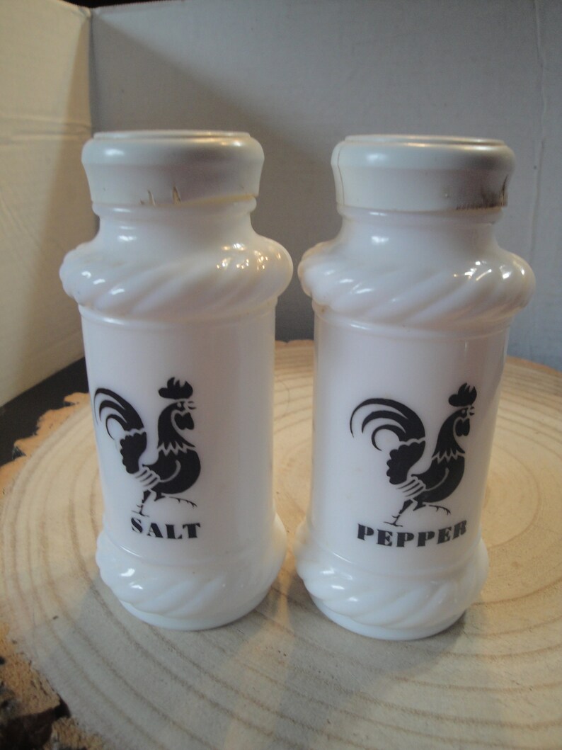 Pode incluir: Saleiro e pimenteiro de cer&acirc;mica branca com um design de galo preto. Os saleiros t&ecirc;m um design de corda em torno do meio e dizem "SALT" e "PEPPER" na parte inferior.