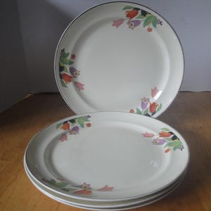 May include: A set of three round, off-white ceramic dinner plates featuring a delicate floral pattern of tulips in shades of red, orange, purple, and green. Each plate has a smooth, glossy finish and a thin, dark rim along the outer edge.