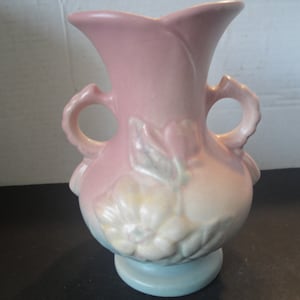 May include: A pink and white glazed ceramic vase with two handles and a floral design. The vase has a light blue base.