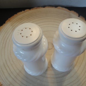 Pode incluir: Um conjunto de dois saleiros e pimenteiros de cer&acirc;mica branca com um design em espiral. Os saleiros t&ecirc;m uma parte superior redonda com v&aacute;rios orif&iacute;cios para dispensar sal e pimenta.