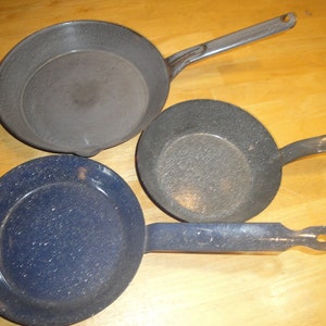 Puede incluir: Tres sartenes vintage de hierro fundido esmaltado. Una es azul con motas blancas, y dos son grises con motas blancas. Las sartenes tienen mangos largos.