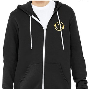 Könnte beinhalten: Schwarzer Kapuzenpullover mit Reißverschluss und weißen Kordeln. Der Hoodie hat ein gelbes Smiley-Gesicht mit Kopfhörern auf der linken Brust.