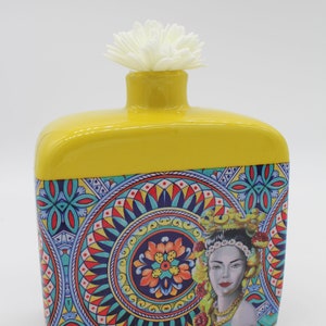 Könnte beinhalten: Gelbe Keramikvase mit einem bunten floralen und geometrischen Muster. Die Vase zeigt das Gesicht einer Frau mit einer Krone aus Früchten und Blumen.