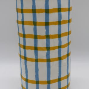 Könnte beinhalten: Eine zylindrische Keramikvase mit weißem Hintergrund und einem Gittermuster aus blauen, gelben und grünen Linien. Die Vase ist etwa 20 cm hoch und hat einen Durchmesser von 10 cm.