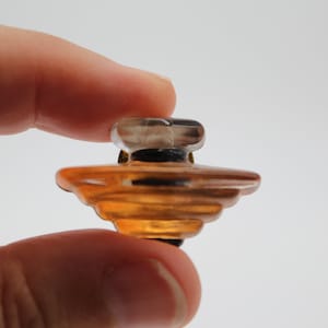 Könnte beinhalten: Eine durchsichtige Glasflasche mit einem gold- und braunen, geschichteten Boden. Die Flasche hat einen durchsichtigen Glasverschluss.