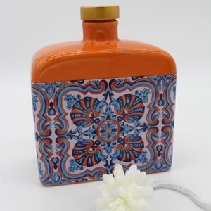 Könnte beinhalten: Orangefarbene Keramik-Diffuserflasche mit blau-weißem Muster. Die Flasche hat einen goldenen Deckel und wird mit einem weißen Diffusorstick geliefert.
