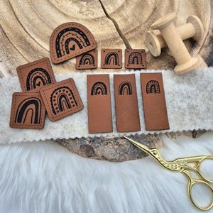 Könnte beinhalten: Ein Set aus neun braunen Leder-Patches mit Regenbogen-Designs. Die Patches sind in verschiedenen Größen und Formen, einige mit Sternen und Herzen.