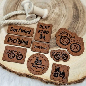 Könnte beinhalten: Neun braune Lederpatches mit schwarzen Nähten und Traktormustern. Die Patches sagen "Dorfkind" und "Dorf Kind".