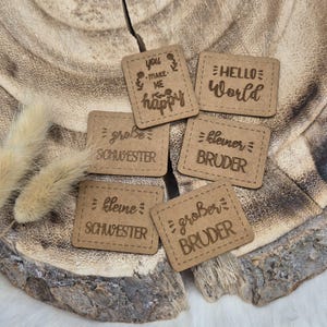Könnte beinhalten: Sechs Holzanhänger mit verschiedenen eingravierten Sprüchen. Die Sprüche lauten: "You make me happy", "Hello World", "Kleine Schwester", "Grosse Schwester", "Kleiner Bruder" und "Großer Bruder".