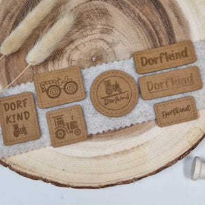 Könnte beinhalten: Sechs braune Holzanhänger mit dem Text "Dorfkind" und einem Traktor-Design. Die Anhänger befinden sich auf einer Holzoberfläche.