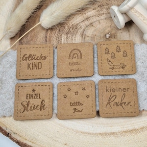 Könnte beinhalten: Sechs quadratische Holzetiketten mit verschiedenen Sprüchen und Designs. Die Etiketten sind braun und haben einen genähten Rand. Die Sprüche lauten "Glückskind", "Little One", "Einzel Stück", "Little Star", "Kleiner Racker" und ein Fuchs mit Bäumen.