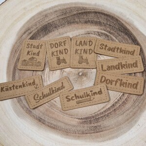 Könnte beinhalten: Neun braune Papieretiketten mit unterschiedlichem Text und Bildern. Die Etiketten sagen "Stadt Kind", "Dorf Kind", "Land Kind", "Stadtkind", "Landkind", "Dorfkind", "Küstenkind", "Schulkind" und "Schulkind".