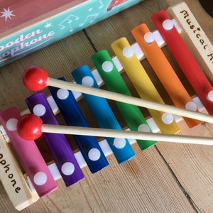 May include: A rainbow-colored wooden xylophone with two wooden mallets. The xylophone has the words "Musical Ava's 1st" and "Xylophone" engraved on the side.