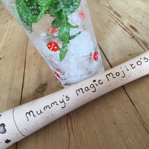 May include: A wooden muddler with the text "Mummy's magic Mojito's!" engraved on it. The muddler is sitting on a wooden surface next to a glass with ice, mint leaves, and red strawberries.