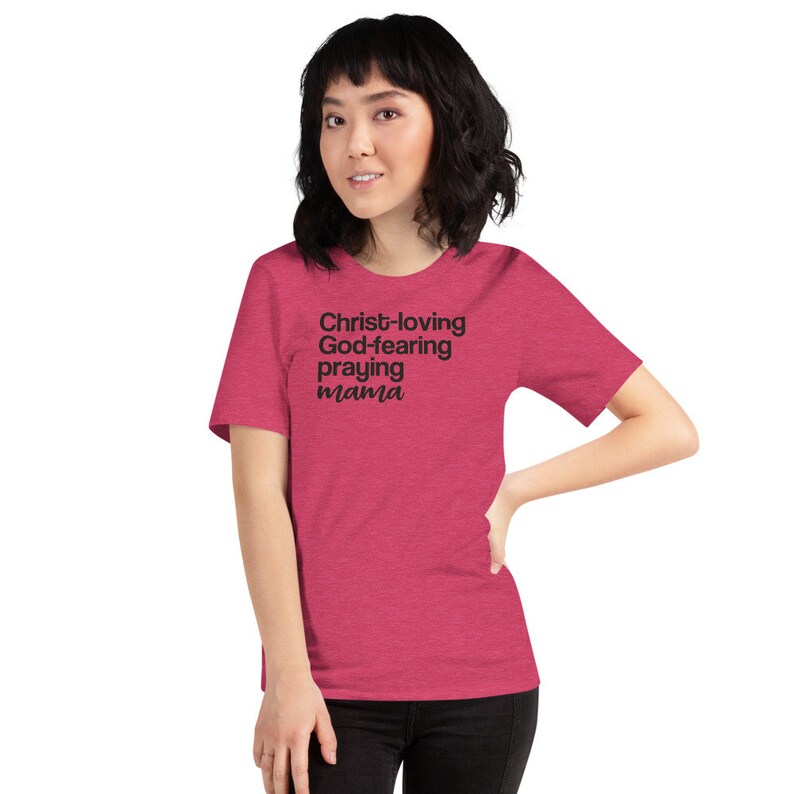May include: A magenta t-shirt featuring the text "Christ-loving God-fearing praying mama" in black. The short-sleeved top is made of a soft fabric.