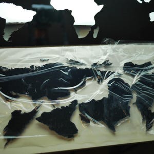 May include: A black world map cutout with a plastic covering. The map is made of a thick, durable material and is perfect for displaying on a wall or desk.