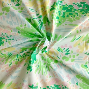 Può includere: Tessuto bianco con un motivo floreale colorato. Il design presenta pennellate verdi, gialle, rosa e blu, creando un aspetto vibrante e artistico. Il tessuto è piegato, mostrando la natura ripetitiva del motivo.