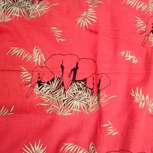 May include: A vibrant coral-red fabric featuring a repeating pattern of dark navy blue elephants standing amidst light beige palm fronds. The textile displays a consistent print of wildlife and tropical foliage across the entire surface area.