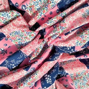 Könnte beinhalten: Rosa und blauer Blumenstoff mit Patchwork-Muster. Der Stoff ist aus einem weichen, leichten Material gefertigt und hat einen dezenten Glanz.