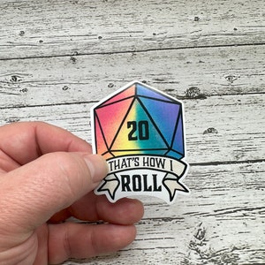 May include: A rainbow-colored 20-sided die with the number 20 printed on it. A banner below the die reads "That's how I roll."