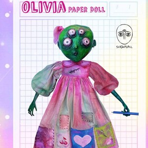 May include: A whimsical paper doll named Olivia with a green face and four eyes, wearing a pink and red dress with patchwork details. The doll holds a blue pencil. Text includes "OLIVIA PAPER DOLL" and "DIGITAL FILE - INSTANT DOWNLOAD".