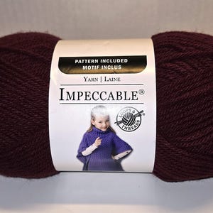 May include: A large ball of Impeccable yarn in a deep burgundy color. The label includes the text "Pattern Included" and a picture of a child wearing a purple garment. The yarn is from Loops & Threads.