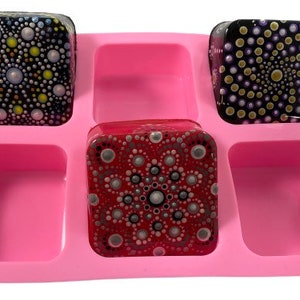 May include: Pink silicone mold with six square cavities. Three of the cavities are filled with square resin pieces with colorful dot patterns. The resin pieces are painted in shades of red, purple, and yellow.
