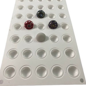 Puede incluir: Molde de silicona blanco con 36 cavidades redondas para hacer manualidades de resina. El molde está lleno de tres círculos de resina coloridos con patrones intrincados.