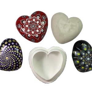 Puede incluir: Cinco cajas en forma de corazón, dos con patrones tipo mandala en morado y dorado, rojo y blanco, y negro y dorado, una caja blanca lisa y una caja blanca lisa con una abertura en forma de corazón.