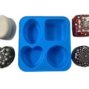 May include: A blue silicone mold with four different shapes: a circle, a heart, a square, and an oval. The mold is used to make soap or other crafts. There are five finished soap bars in the image, each with a different mandala design.