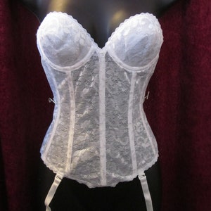 May include: White lace corset with a sweetheart neckline and boning details. The bustier features a delicate floral lace pattern and includes attached garter straps. The garment is displayed on a black mannequin.