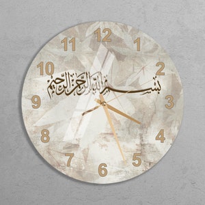 Op de afbeelding: Een ronde, witte klok met gouden Arabische cijfers en wijzers. De wijzerplaat heeft een verweerde, vintage uitstraling met een wit en gouden abstract ontwerp. De wijzerplaat bevat ook de Arabische tekst "بسم الله الرحمن الرحيم" in goud.