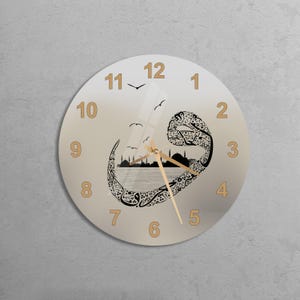 May include: A round glass clock with a beige background and gold numbers. The clock face features a black and white design of a mosque with birds flying above it. The clock hands are gold.