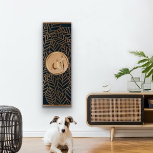 May include: A vertical wall art piece with a dark blue background and gold leaf design. The center of the art piece features a gold circle with the Arabic word "Allah" written in gold.