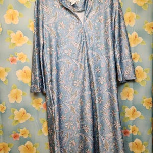 May include: A light blue long-sleeve robe featuring a repeating floral and paisley pattern in shades of pink, white, and green. The garment has a full-length front zipper closure and a label at the neckline that reads Gerry.
