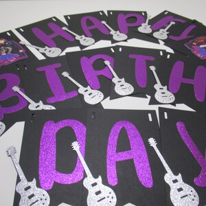 May include: Purple glitter letters spelling "Happy Birthday" with silver glitter guitar cutouts on black cardstock.