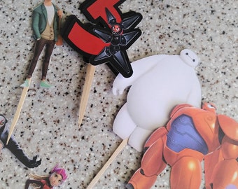 Op de afbeelding: Een set van zes taarttoppers met personages uit de animatiefilm Big Hero 6. De toppers zijn Baymax, Hiro Hamada, Honey Lemon, Go Go Tomago, Wasabi No-Ginger en Fred. De toppers zijn gedrukt op karton en hebben houten stokjes die aan de achterkant zijn bevestigd.