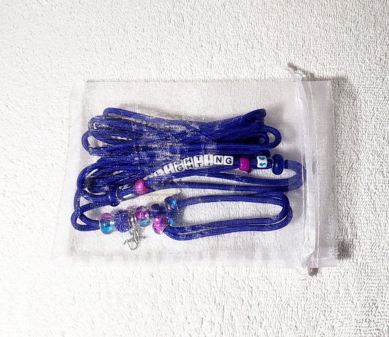 May include: A blue and purple beaded necklace with a silver clasp and the word "FIGHTING" spelled out in white letter beads. The necklace is in a clear plastic bag.
