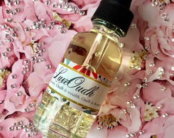 Może przedstawiać: Przezroczysta butelka ze szkła z czarną zakrętką z kroplomierzem i białą etykietą z napisem "Luxe Oudh" oraz tekstem "Luxury. Oudh is wealth. Oudh is beauty." Butelka stoi na różowo-białym tle z kwiatami i małymi, przezroczystymi kryształkami rozrzuconymi wokół.