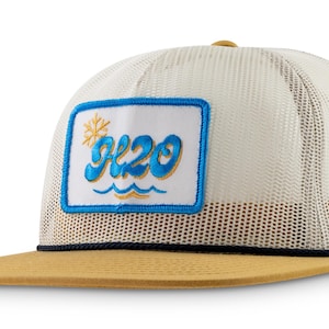 Peut inclure: Un chapeau de camionneur en maille blanche et beige avec un patch brodé bleu et jaune qui dit "H2O" avec un flocon de neige et des vagues.