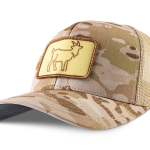 Può includere: Un cappello da camionista mimetico con una toppa marrone che presenta una silhouette gialla di una capra. Il cappello ha una parte posteriore in rete.