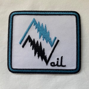 May include: A white embroidered patch with a blue and black mountain design. The text "vail" is embroidered in black below the mountains.