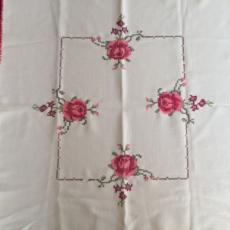 Puede incluir: Mantel blanco con un marco cuadrado bordado con cuatro rosas rosas y hojas verdes.