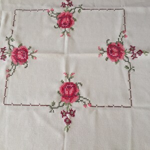 Puede incluir: Mantel blanco con un borde bordado marr&oacute;n y cuatro rosas rosas en las esquinas.