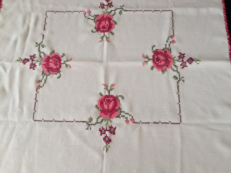 Puede incluir: Mantel blanco con un borde bordado marr&oacute;n y cuatro rosas rosas en las esquinas.