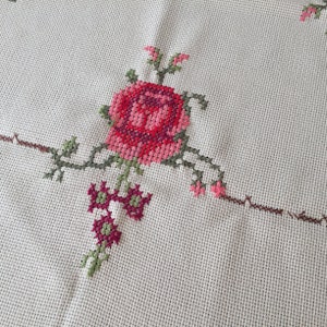 Puede incluir: Primer plano de una tela blanca con un dise&ntilde;o de rosa bordada en rosa y verde.